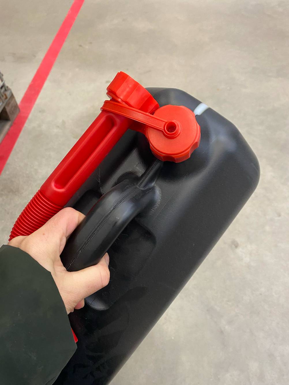 Eine Hand hält einen getesteten Benzinkanister vor einen hellen Boden.