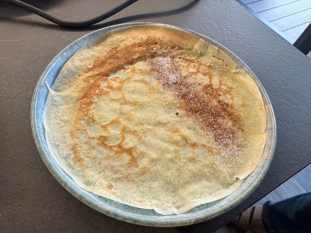 Ein fertiger Crêpe mit Zimt und Zucker liegt auf einem Teller