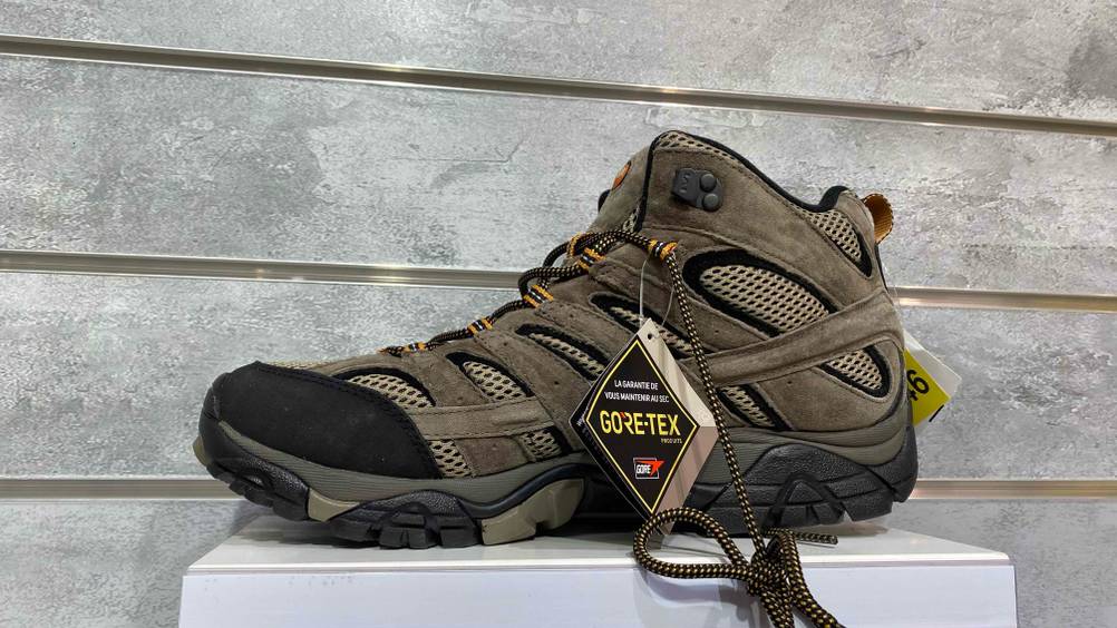 Ein getesteter Bergschuh für Herren von der Seite auf einem weißen Sockel.