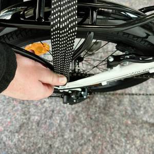 Zu sehen ist der montierte Gepäckträger des Bergsteiger Windsor mit einer Hand, die ein Spanngummi über das Hinterrad zieht.