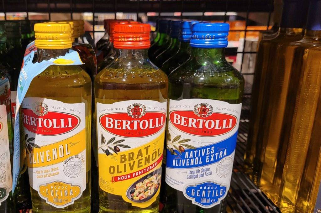 Im Test: Mehrere Flaschen Bertolli-Ölivenöl in verschiedenen Sorten stehen in einem Regal.
