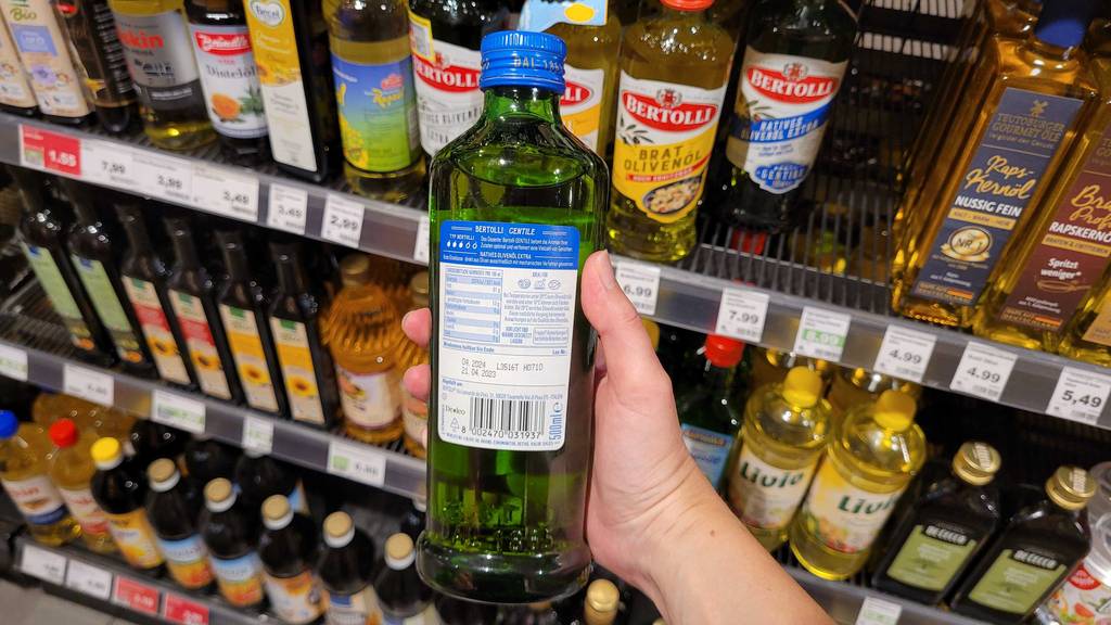 Im Test: Hand hält eine Flasche Bertolli-Olivenöl mit der Rückseite nach vorn vor ein Verkaufsregal.