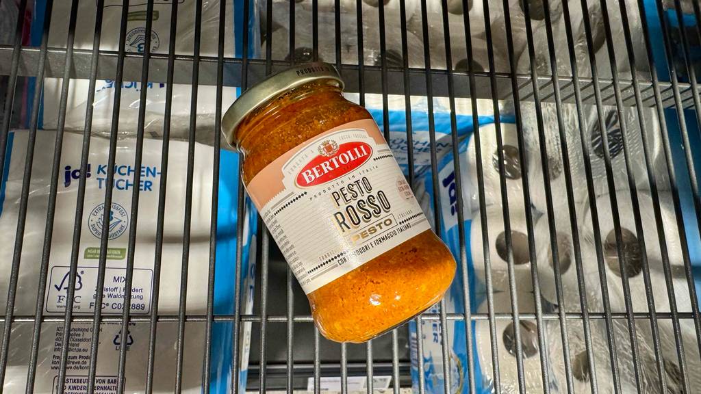 Ein Glas getestetes Pesto Rosso liegt in einem Gitterregal, darunter sind Küchenrollen zu sehen.