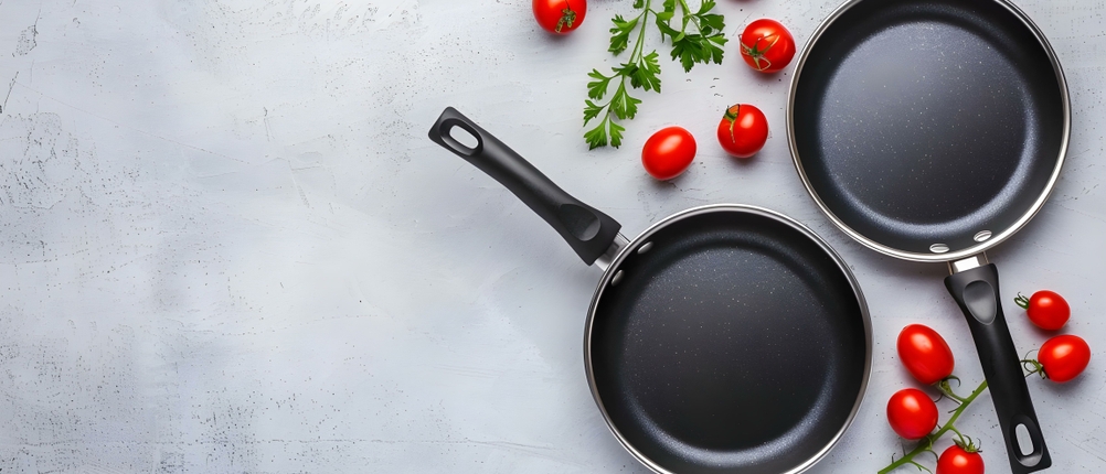 Beschichtete Pfannen im Test: Zwei beschichtete Pfannen wurden auf einer grauen Arbeitsplatte platziert. Daneben befinden sich Tomaten.