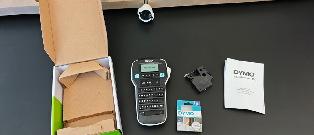 Ein Dymo Labelmaker 160 liegt samt seiner Verpackung auf einem Tisch.