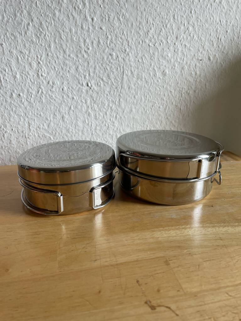 Camping-Kochgeschirr aus Edelstahl im Test: Das 2-er-Set steht auf einer Holzfläche vor einer weißen Wand.