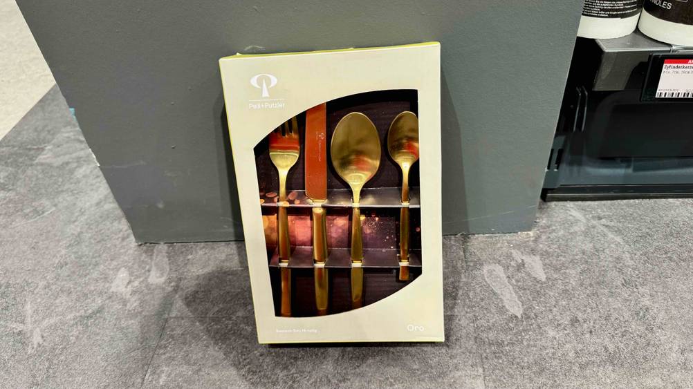 Ein Packung des Besteck (gold) im Test lehnt an einer grauen Wand auf dem Boden.