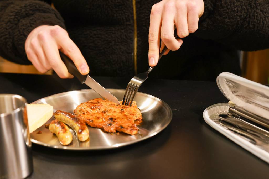 Camping-Besteck-Set-Test: Fleisch wird auf Teller mit Besteck-Set geschnitten.