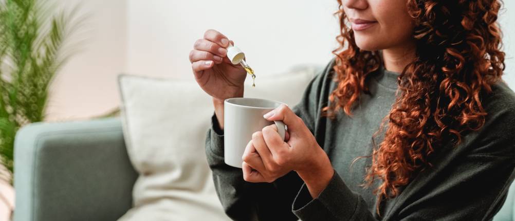 CBD-Öl kaufen: Eine junge Frau gibt CBD-Tropfen in eine Tasse.