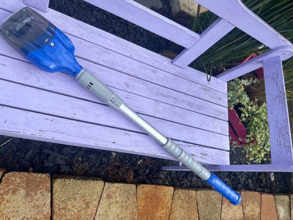 Poolsauger im Test: ein blau-graues, batteriebetriebenes Modell inklusive Alu-Teleskopstiel befindet sich auf einer violettfarbenen Holzbank im Außenbereich.