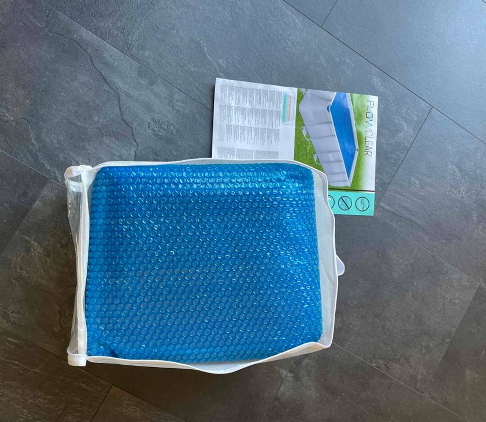 Eine getestete Poolabdeckung in ihrer geöffneten Originalverpackung auf einem dunklen Boden.