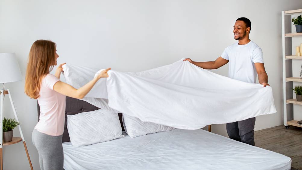 ein Pärchen schüttelt eine Bettdecke auf und macht das Bett