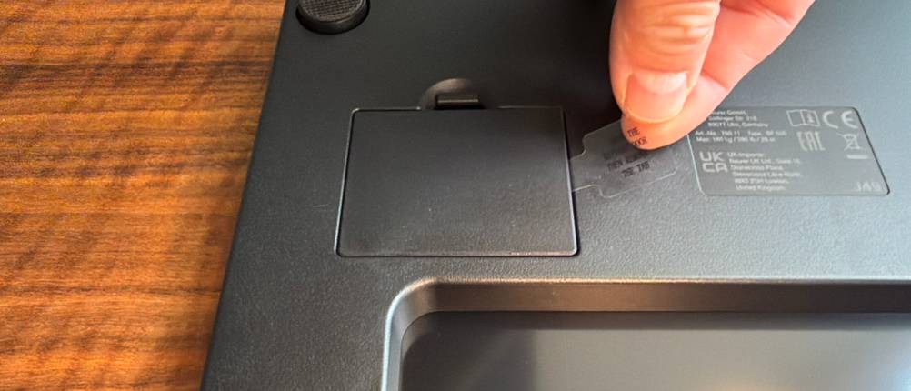 Eine Hand entfernt ein Stück Plastik vom Batteriefach der Beurer BF 500.