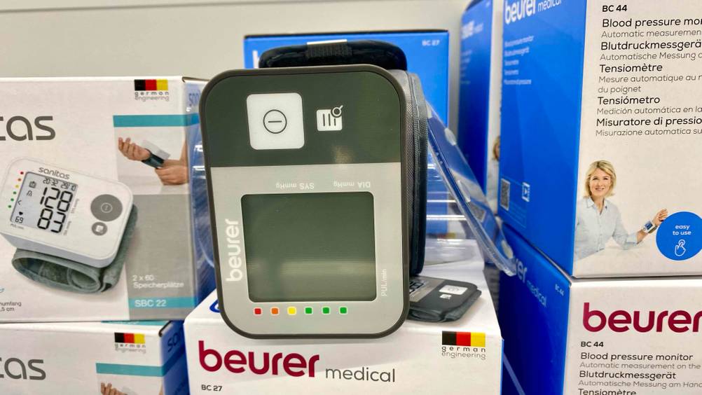 Im Test: Nahaufnahme des Bildschirms und der Bedienelemente eines Beurer-Blutdruckmessgerät auf der Seite liegend von vorne auf einem Originalkarton.