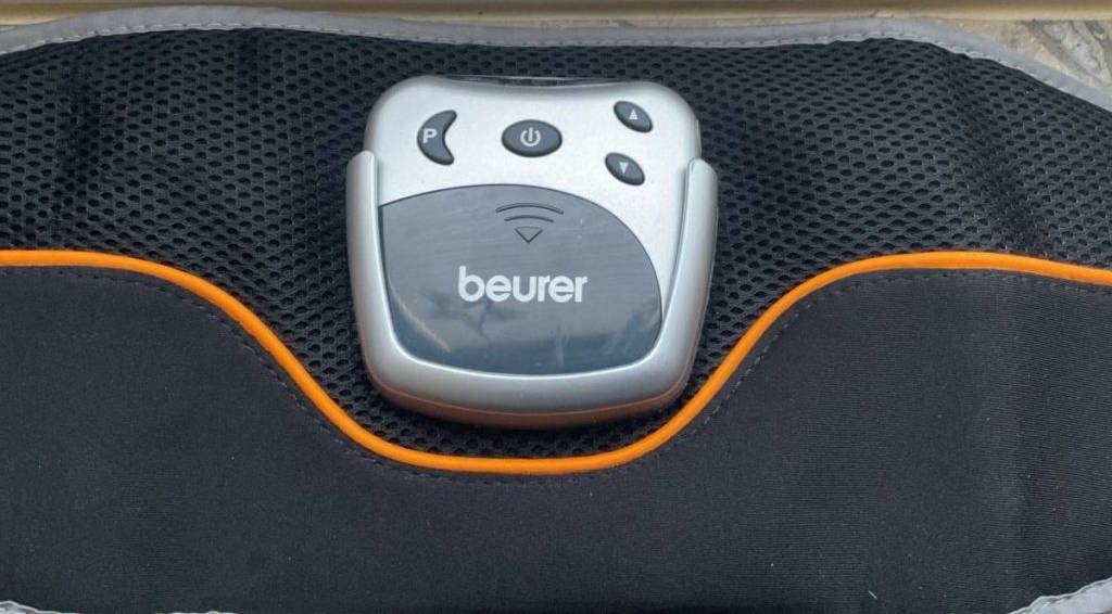 Baumuskelgürtel-Test: Detailaufnahme der silbernen Einschalt- und Regler-Einheit inklusive Programm-Taste von einem schwarzen Modell mit oranger Zierborte.