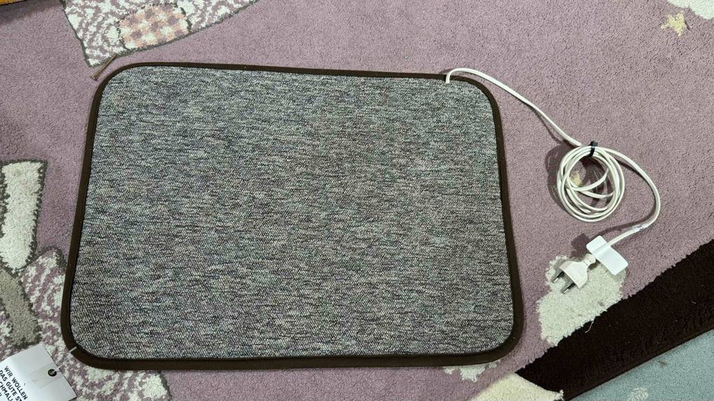 Heizteppiche im Test: Ein graues Modell inklusive Kabel liegt auf einem Teppich in Altrosa.