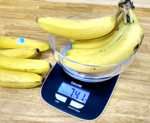 Auf einer schwarzen Küchenwaage liegen Bananen in einer Glasschale, die Waage zeigt 741 Gramm an.