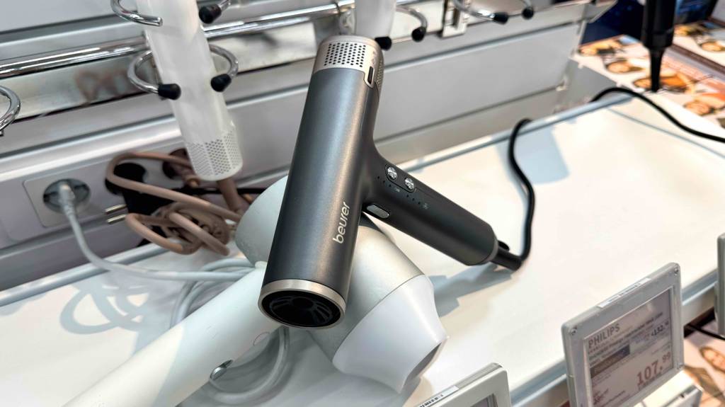 Auf einem weißen Haartrockner liegt ein grauer leichter Haartrockner im Test auf einem Ausstellungsregal im Verkaufsbereich.