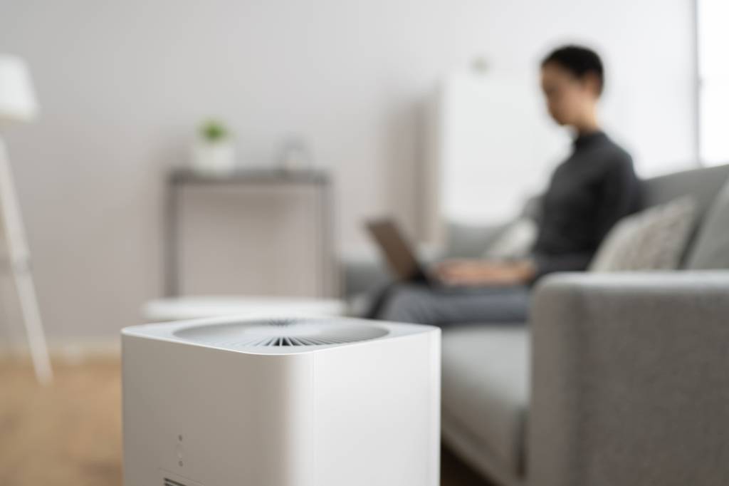 Beurer-Luftbefeuchter im Test: Ein Gerät steht in Fokus, während im Hintergrund auf einer grauen Couch eine Person mit Laptop sitzt.