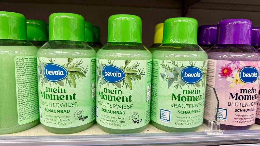 In einem Verkaufsregal stehen mehrere Kunststoffflaschen mit veganem grünem Schaumbad nebeneinander.