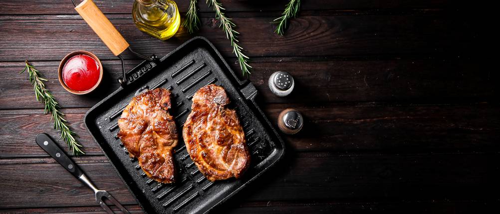 Bialetti-Pfanne-Test: fertig gebratene Steaks in einer Grillpfanne umgeben mit Kräutern und Gewürzen