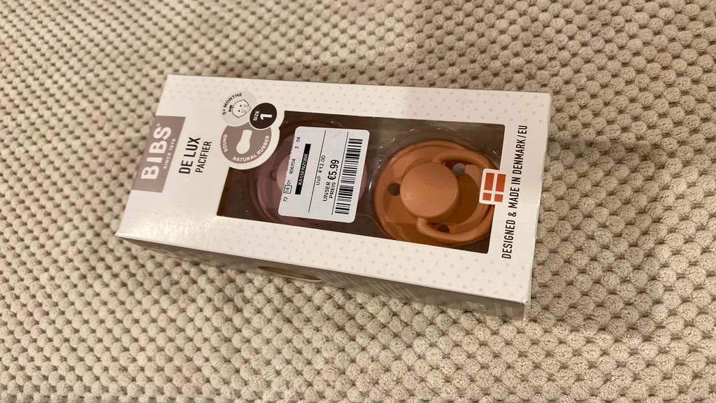 Bibs-Schnuller-Test: eine beigefarbene Verpackung, mit Sichtfenster und Preisetikett, liegt auf einem beigefarbenen Stoff.