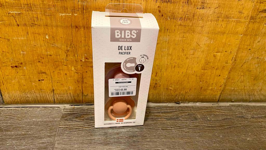 Bibs-Schnuller im Test: eine beigefarbene Verpackung mit Sichtfenster, hinter dem zwei Schnuller zu sehen sind, steht auf einer Holzoberfläche.