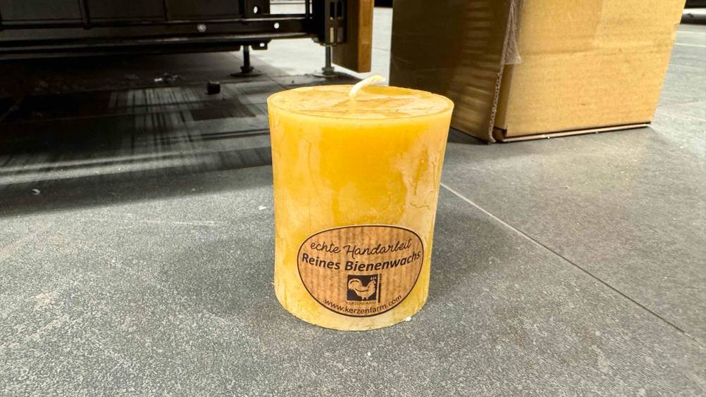 Auf einem grauen Boden steht eine Bienenwachskerze im Test.