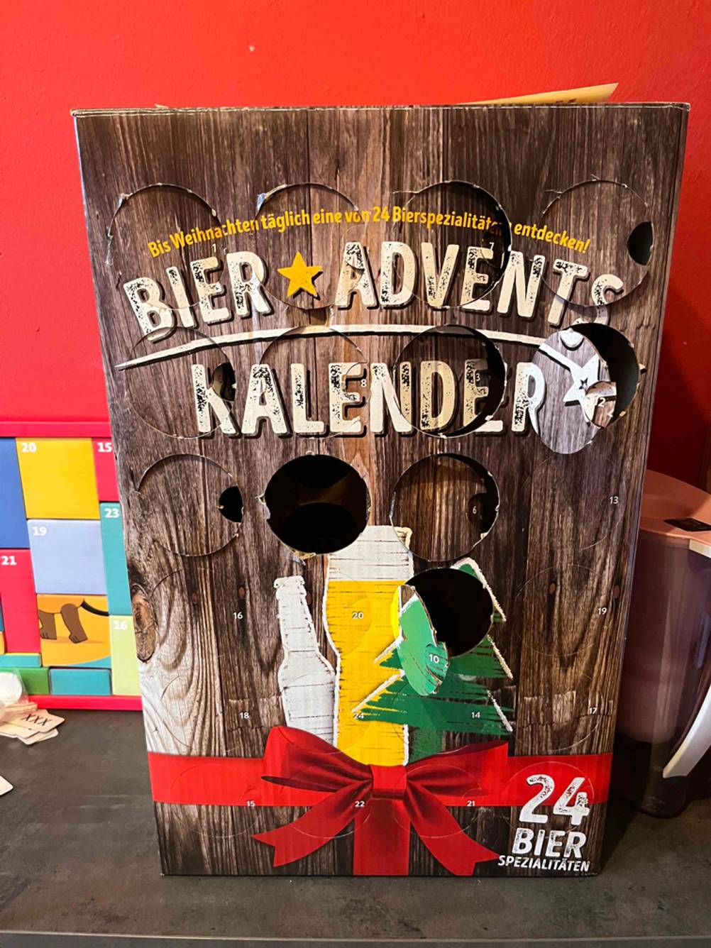 Ein getesteter Bier-Adventskalender von vorne vor einer roten Wand.