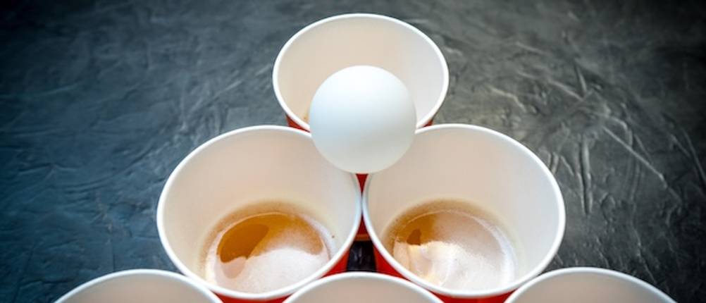 Ansicht von oben auf eine Becher-Pyramide mit einem weißen Tischtennisball auf einem getesteten Bier-Pong-Tisch.