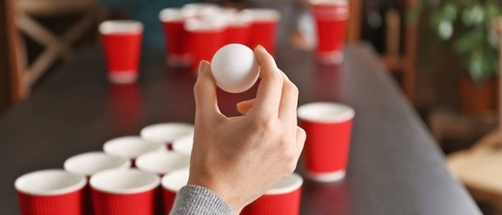 Bier-Pong-Tisch-Test: Eine Hand wirft einen weißen Tischtennisball auf einem Bier-Pong-Tisch mit roten Bechern.