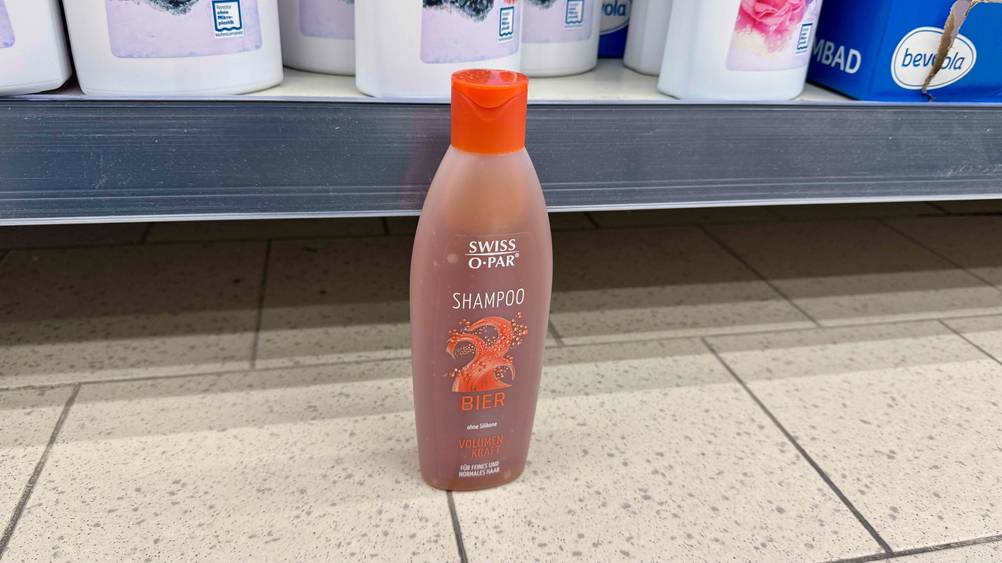 Vor einem Regal steht eine Flasche Bier-Shampoo im Test auf dem Boden.