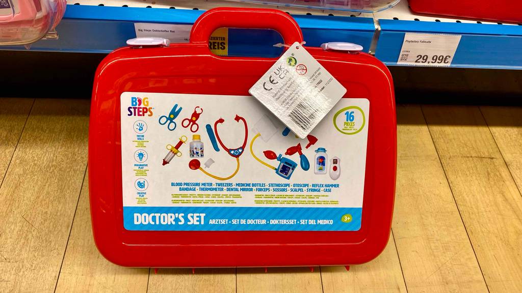 Im Test: Arztkoffer für Kinder in Rot mit Beschreibungsaufkleber steht an ein Verkaufsregal gelehnt.