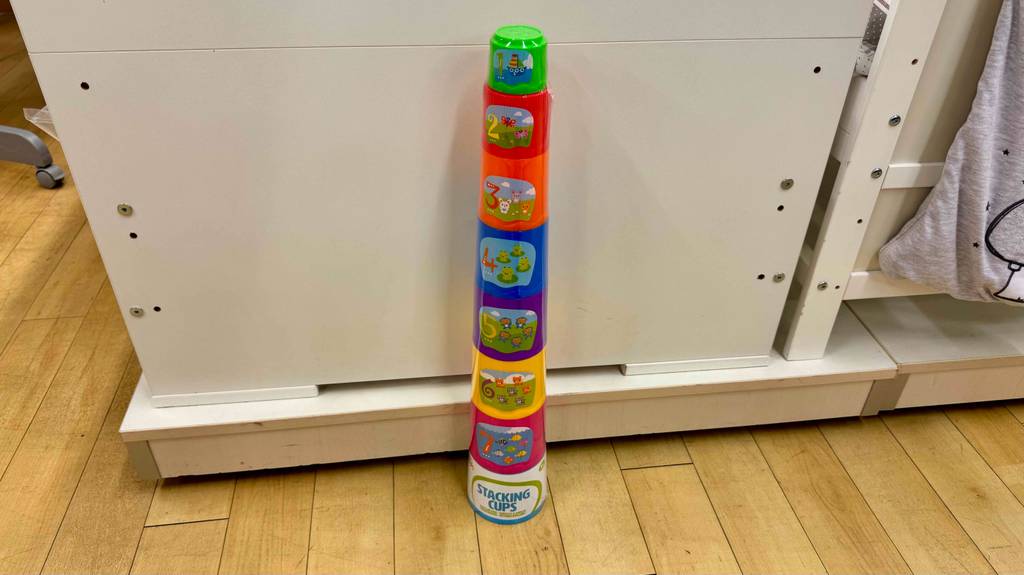 Stapelbecher-Test: Die bunten Stapelbecher mit Nummerierung und Nummernbildern stehen vor einem weißen Kinderbett.