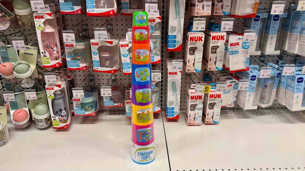 Die bunten, mit Nummerierung und Nummernbildern bedruckten, getesteten Stapelbecher stehen vor einem Regal mit Kleinkinder-Produkten.