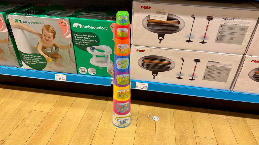 Die bunten, mit Nummerierung und Nummernbildern versehenen Stapelbecher im Test stehen vor einem Regal mit Zubehör für die Kleinkinderpflege.