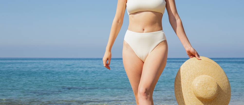Bikini High Waist im Test: Frau im High-Waist-Bikini und Sonnenhut am Strand.