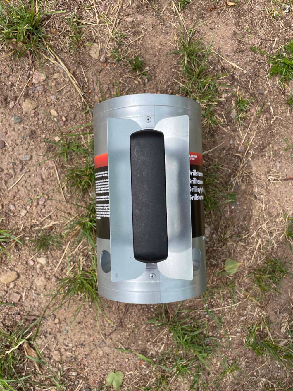 Ein Anzündkamin im Test liegt mit dem Griff nach oben auf trockener Erde.