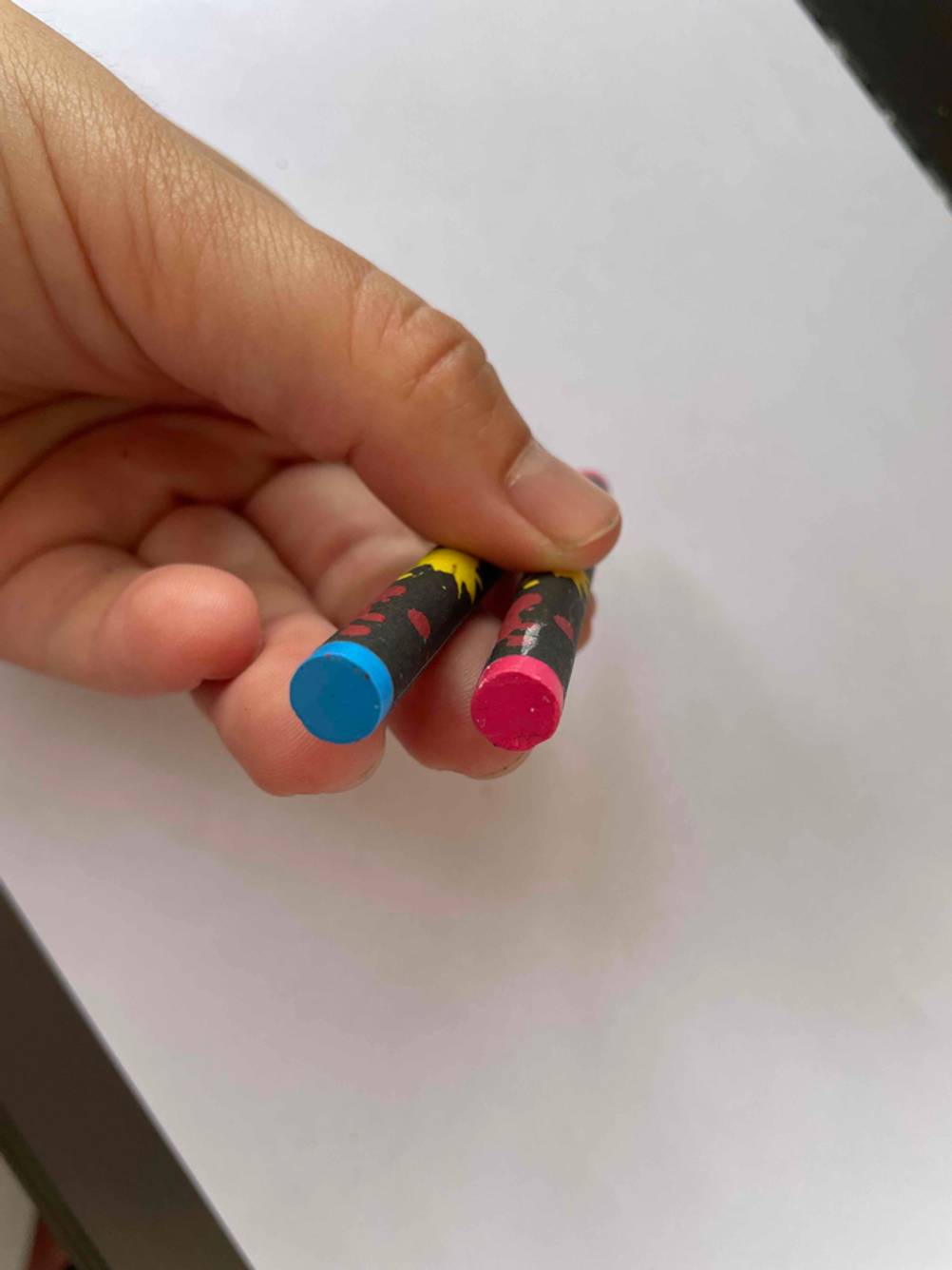 Im Test: Eine Hand hält das Ende zweier Wachsmalstifte vor ein weißes Blatt.