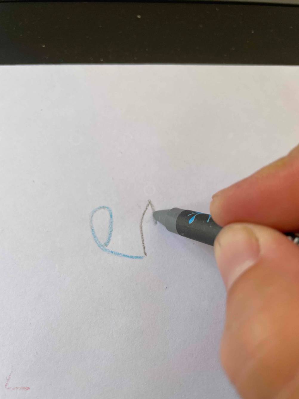 Wachsmalstifte getestet: Eine Hand malt mit einem grauen Stift auf ein weißes Papier.