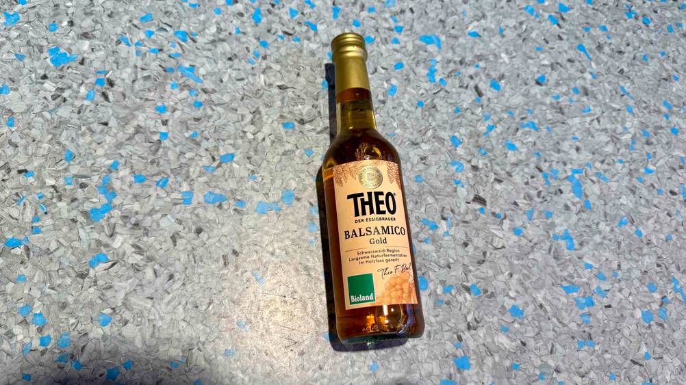 Auf einem blau-grauen Boden liegt eine Flasche des getesteten Bio-Balsamico-Essig.
