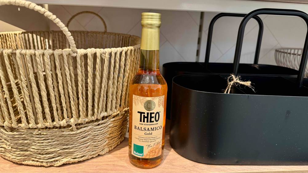 Ein Bio-Balsamico-Essig im Test in einem Regal neben Körben stehend.