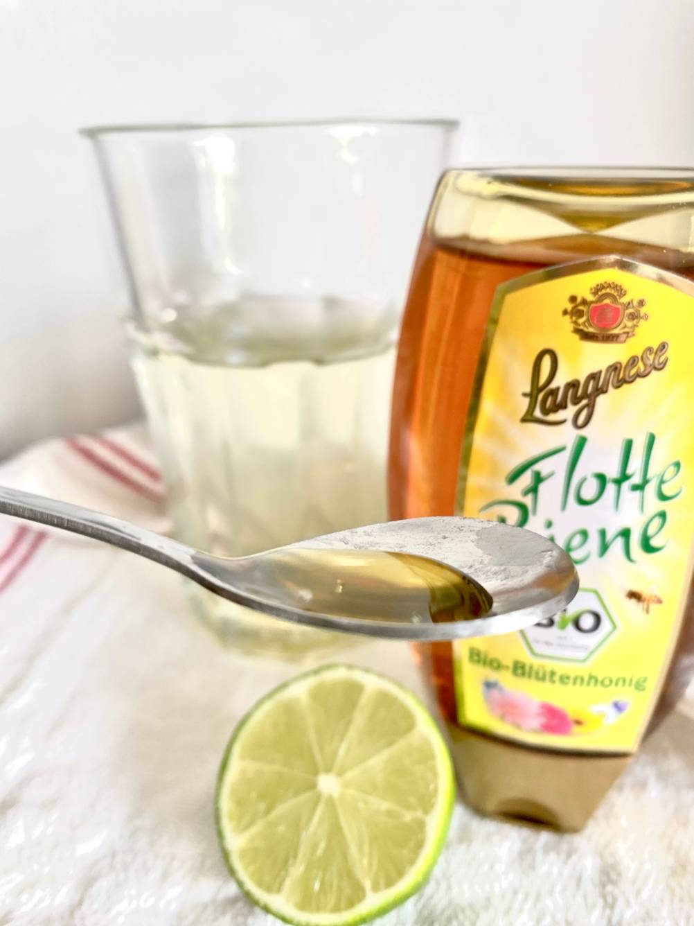 Im Test: Ein Löffel mit Bio-Honig, im Hintergrund eine Flasche Honig, ein Glas und eine Limette.