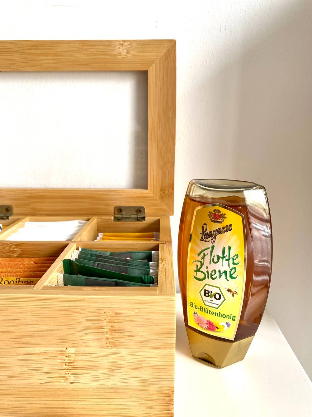 Neben einer geöffneten Teebox steht eine Flasche des getesteten Bio-Honigs.