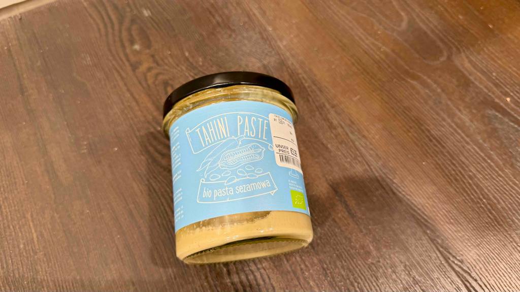Ein Glas Tahini liegt zum testen auf einer Holzfläche.