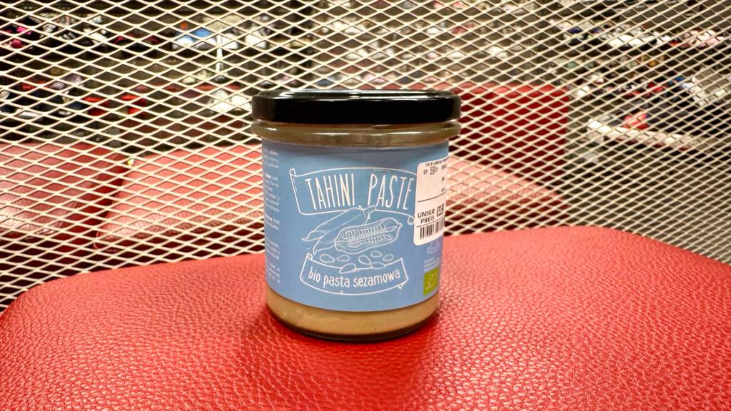 Frontansicht eines Glases getestete Tahini, das auf einer roten Lederfläche steht.