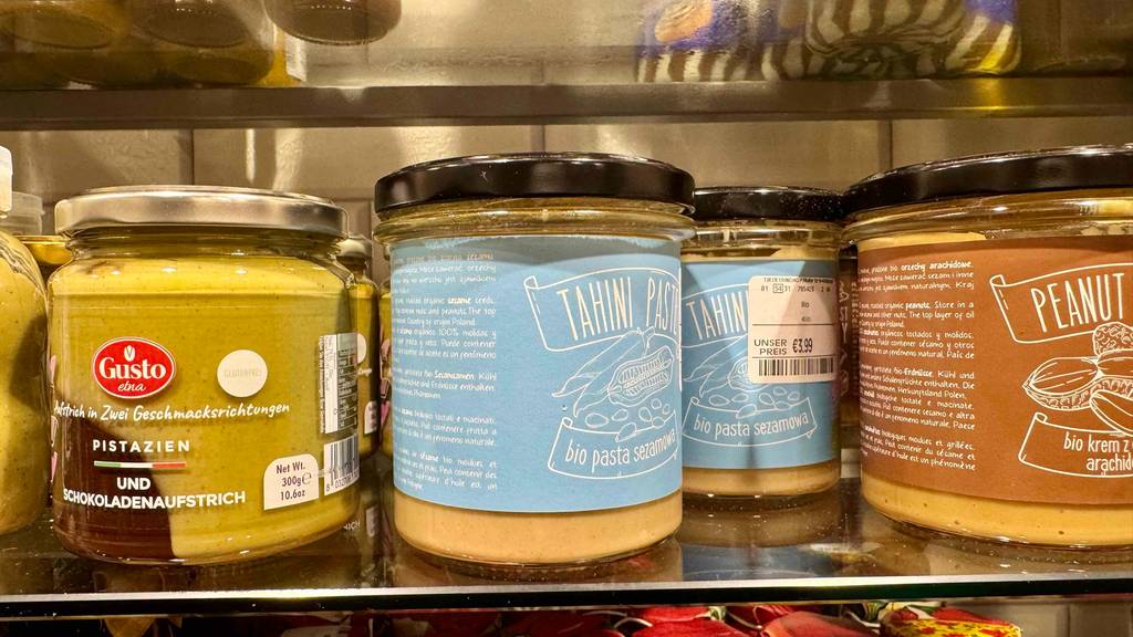 Tahini im Test: Mehrere Gläser stehen zwischen anderen Produkten in einem Regal, das vordere mit Seitenansicht.