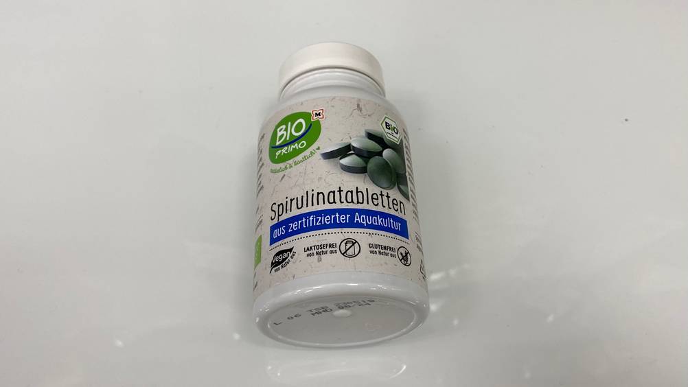 Spirulina-Tabletten-Test: Nahaufnahme des Bodens einer Dose Spirulina-Tabletten auf einer hellen Fläche.