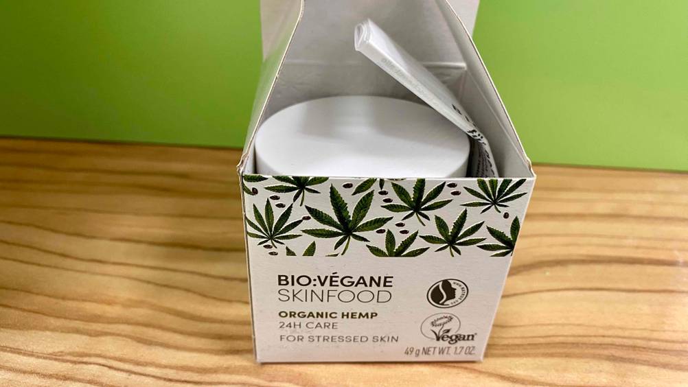 Hanfcreme getestet: Eine geöffnete Packung mit Fokus auf die Dose darin auf einer Holzfläche.