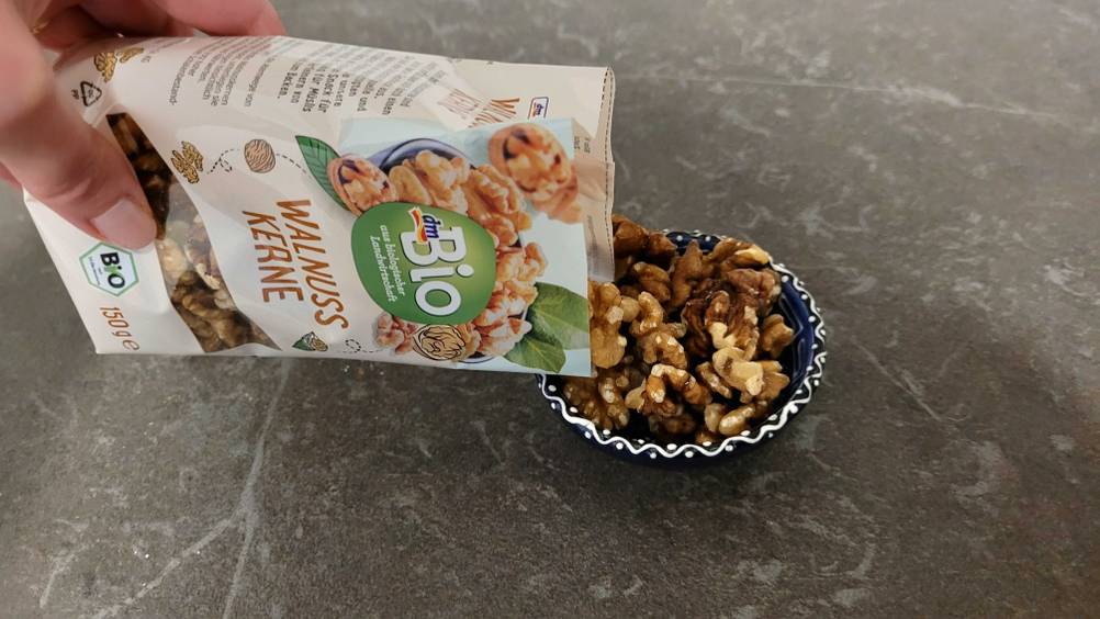 Bio-Walnüsse im Test: Eine Hand hält eine Packung und schüttet den Inhalt in eine kleine Schale.
